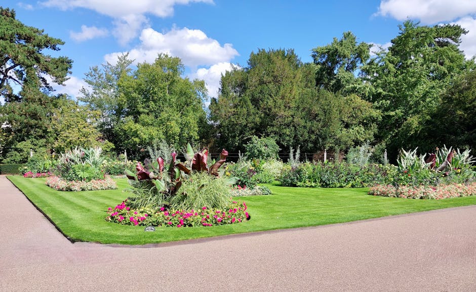 A well-maintained public garden featuring neatly trimmed green lawns and flower beds with colorful blooms, including pink, purple, and white flowers. The garden showcases a variety of plants, such as 